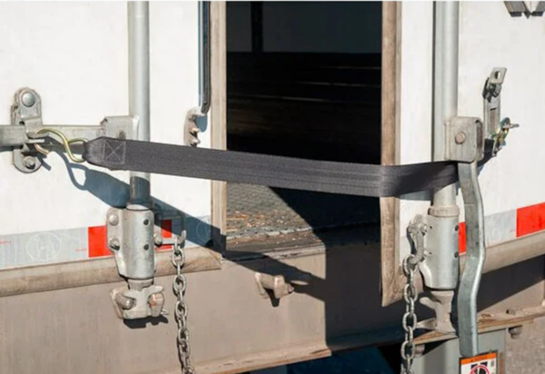 Close-up of a truck's rear cargo door secured with a safety strap and locking mechanisms, emphasizing proper cargo handling and safety.